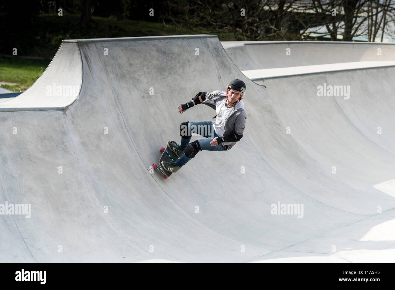Eine ausgereifte Skateboarder tragen Sicherheitseinrichtungen an konkreten Wellen Skateboard Park in Newqay in Cornwall. Stockfoto