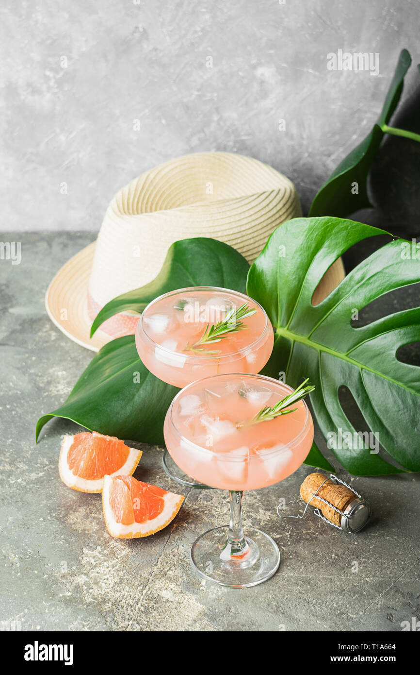 Trinken grapefruit Rosmarin und Eis in zwei eleganten Glas Pokale auf dem Hintergrund der tropischen grünen Blätter und Hüte. Stockfoto