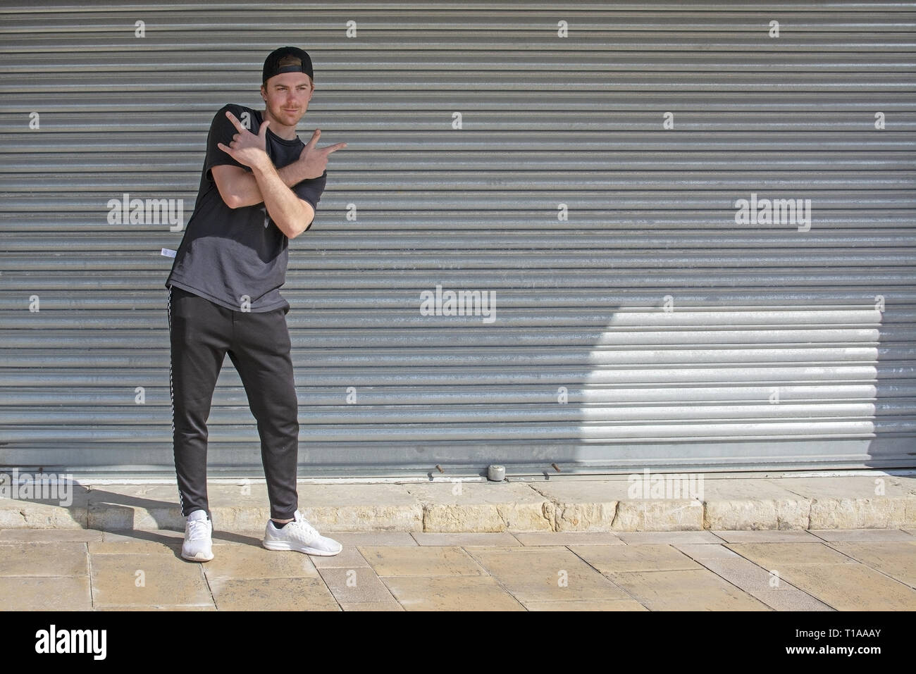 Junge casual Sportlich gekleideter Mann mit Kappe nach hinten in Schwarz gegen Wellblech wall street style Stockfoto