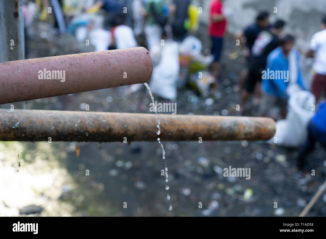 Abwasser durch ein Rohr aus einem Slum eminating Siedlung am Rande eines Flusses in Cebu City, Philippinen Entlastung. Freiwillige sind Müll Reinigung von t Stockfoto