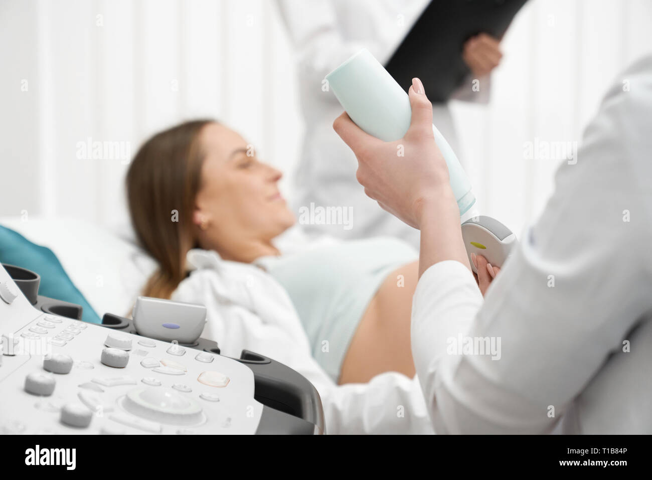 Nahaufnahme des modernen Ultraschallgerät. Arzt Haltevorrichtung, glückliche schwangere Frau liegen in der medizinischen Büro auf Prüfung. Sonographie Diagnose in der eigenen Klinik. Stockfoto