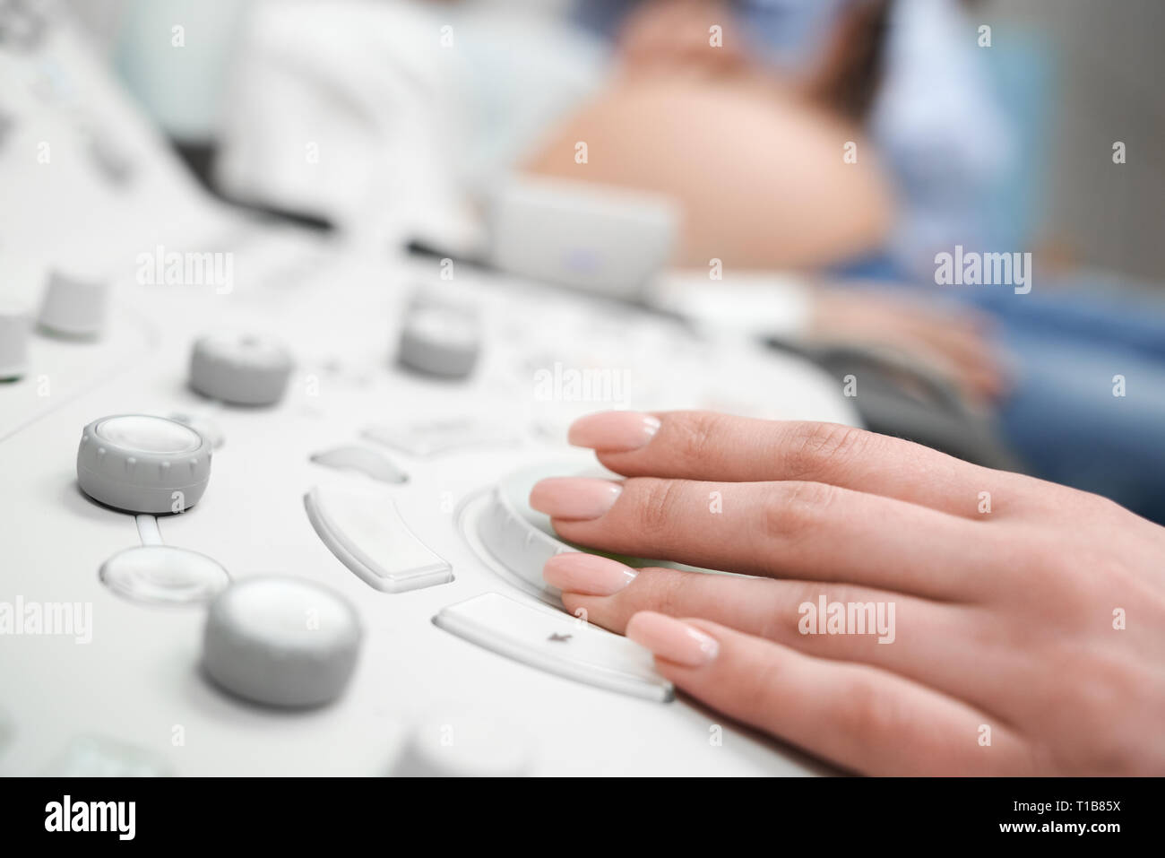 Hand der Arzt auf Ultraschallgerät schließen oben. Krankenschwester, Prüfung der Bauch der schwangeren Frau. Zukünftige Mutter auf der Beratung in der Medizinischen Klinik. Stockfoto