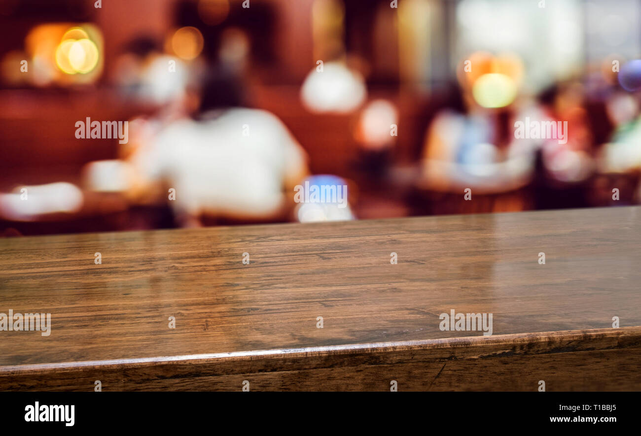 Holz Tisch mit Leuten Abendessen im Restaurant blur Hintergrund. Leer Perspektive Hartholz bar mit blur Coffee Shop mit bokeh Licht, Mock up für die Anzeige Stockfoto