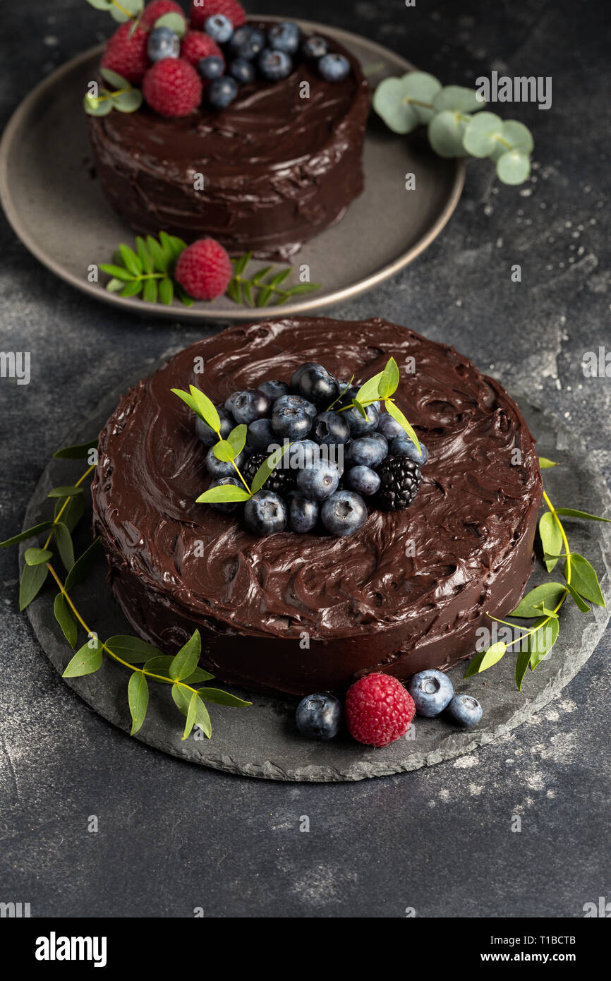 Schokolade Kuchen mit Beeren und grüne Blätter auf der grauen Platte, frische Himbeeren und Blaubeeren in der Nähe von auf dunklem Hintergrund. Konzept der Holiday Dessert Stockfoto
