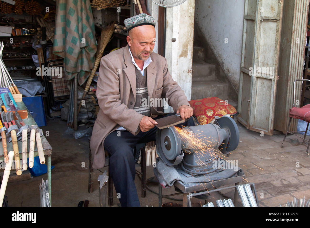Uigurischer Mann außerhalb der Werkstatt Messer schärfen. Kashgar Altstadt, Xinjiang Autonome Region, China. Stockfoto