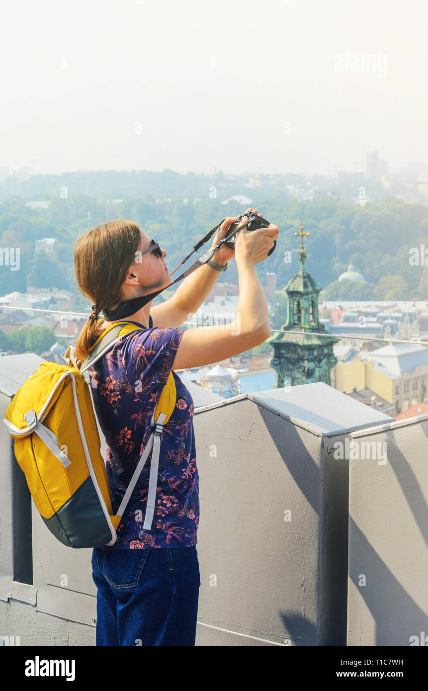 Junge Mädchen touristische Fotograf mit einem gelben Rucksack nimmt Bilder von Sehenswürdigkeiten. Travel Concept. Panorama der Altstadt Stockfoto