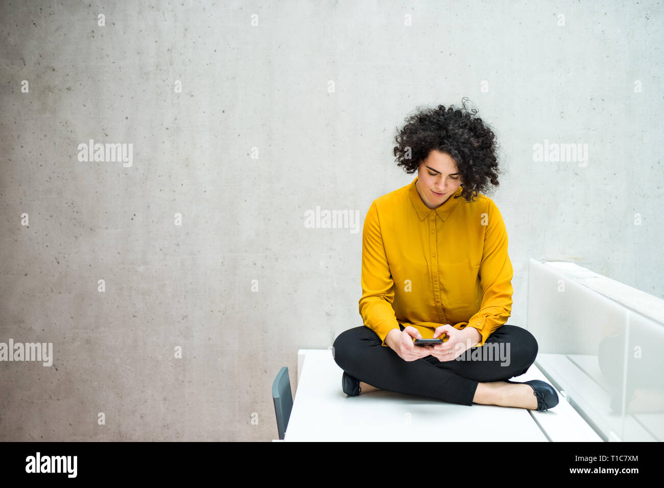Junge student oder Geschäftsfrau mit Smartphone sitzen am Schreibtisch im Zimmer in einer Bibliothek oder im Büro. Stockfoto