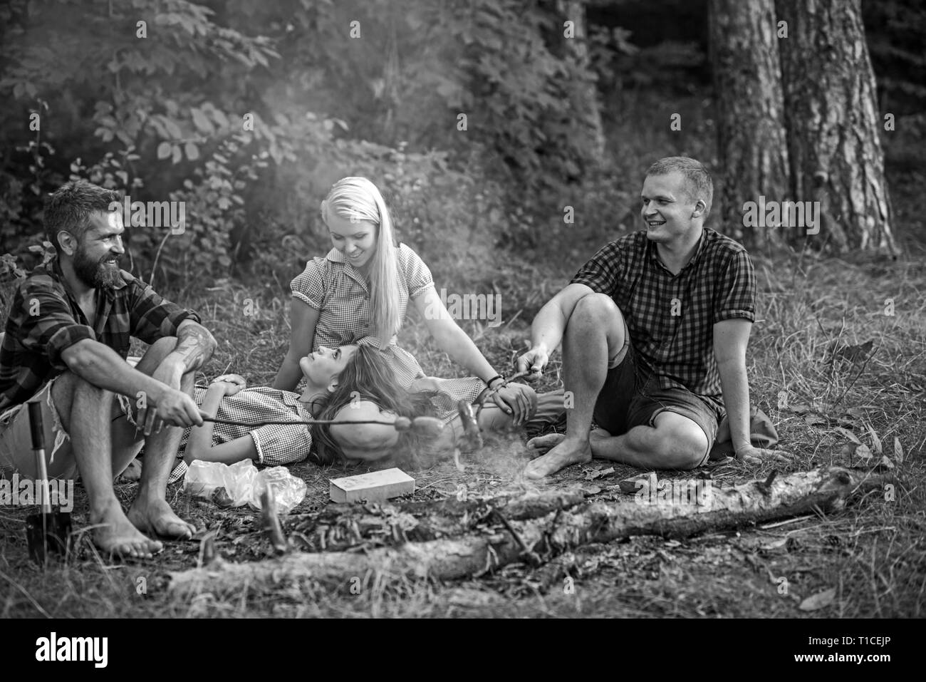 Gruppe von Freunden Camping in Wäldern. Lächelnde Menschen reden um Lagerfeuer. Männer in holzfäller Hemden kochen Würstchen Stockfoto