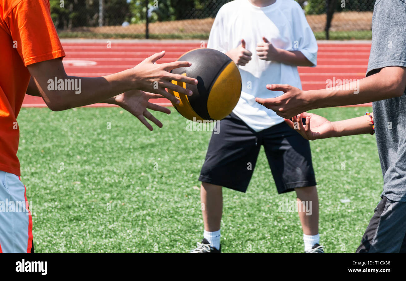 Drei High School Athleten sind seitlich verdrehen werfen einen Medizinball bei der Stärke der Praxis. Stockfoto