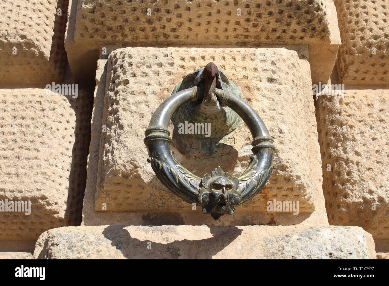 Bronzering, der im Schnabel eines Adlers auf der rustizierten Steinfassade des Palastes Karls V. in der Alhambra, Granada, gehalten wird Stockfoto