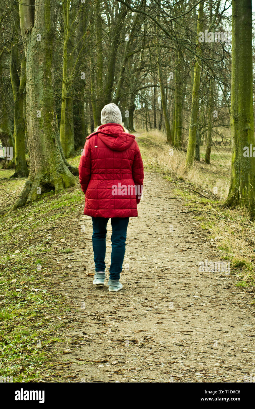 Frau im roten Mantel allein auf einem Pfad in der Natur Stockfoto