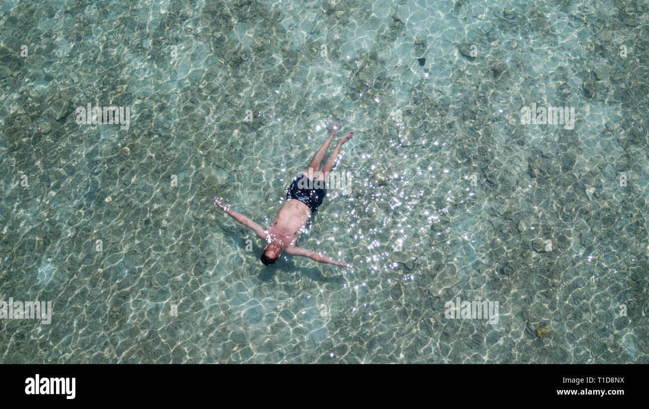 Man schwimmend auf dem Wasser im blauen Ozean. Entspannt Mann auf seine Ferien im Meer Blick von oben. Entspannen Konzeption Stockfoto