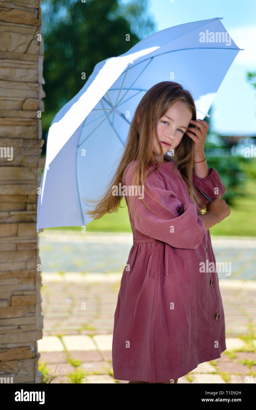 Portrait von schönen Mädchen. Kind in Burgund Kleid hält ein Dach über dem Kopf in hellen, sonnigen Tag. Mode Stockfoto