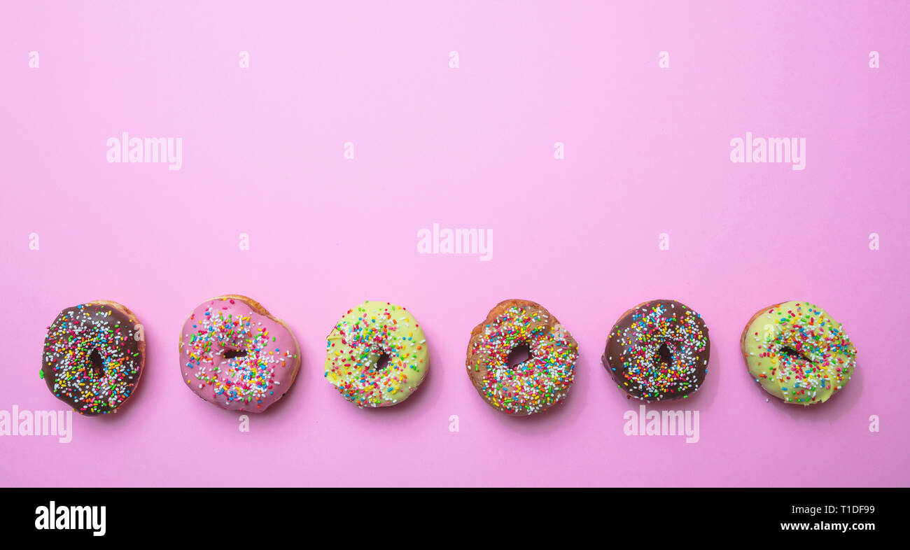 Donuts sortiert. Donuts mit bunten Streuseln und Vereisung auf rosa Hintergrund, Ansicht von oben, kopieren Raum Stockfoto