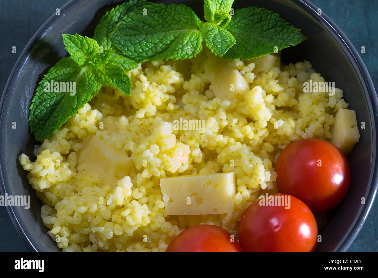 Millet Porridge mit Käse in einer Schüssel mit Tomaten und Minze. Stockfoto