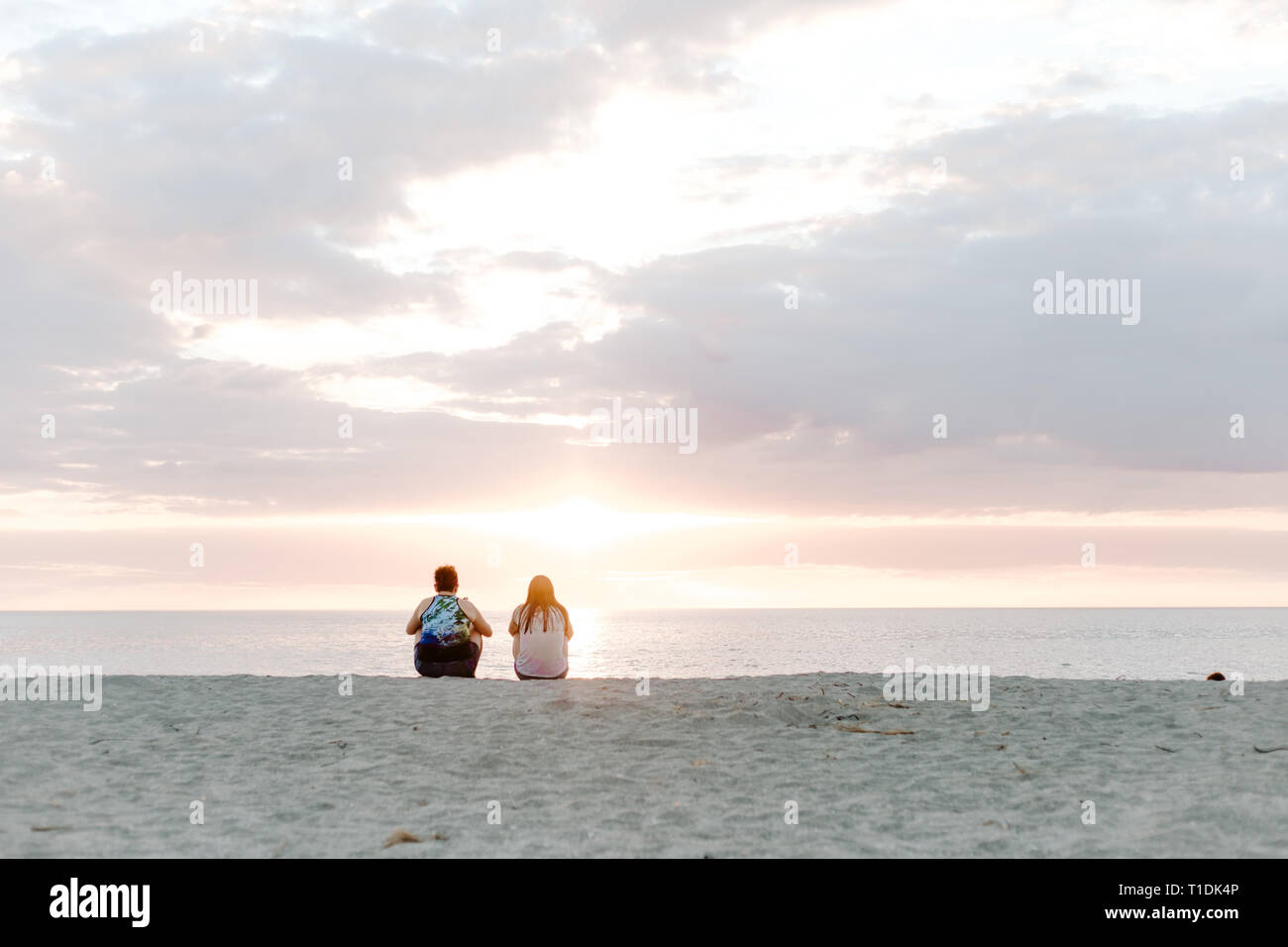 Zwei Leute, die schönen und heiteren Sonnenuntergang über dem Meer Horizont beim Sitzen im Sand am tropischen Strand Stockfoto