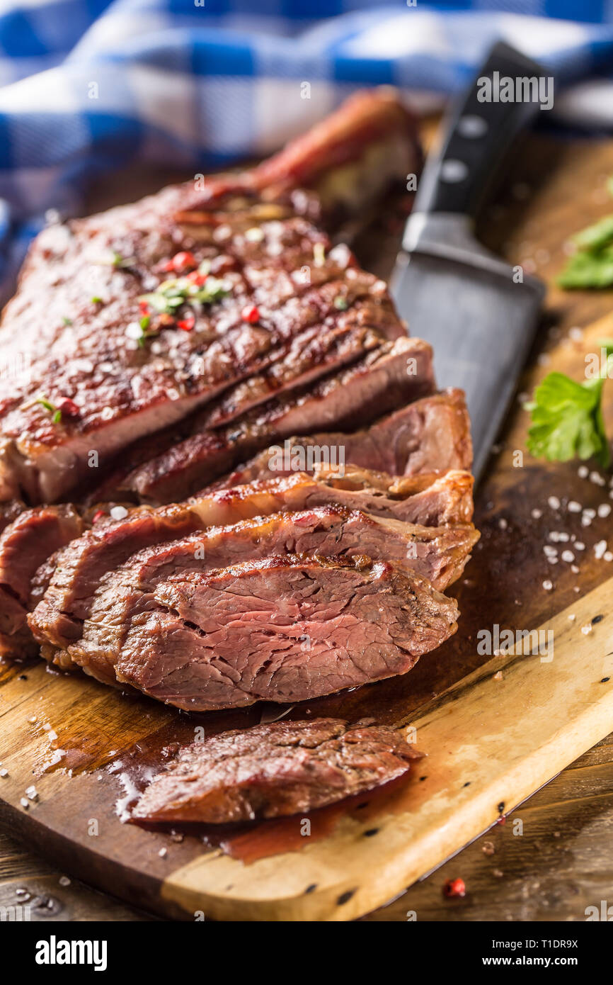 Frisch gegrillten Tomahawk Steak auf schiefer Teller mit Salz, Pfeffer, Rosmarin und Petersilie Kräuter. In Scheiben geschnittene Stücke von saftigen Rindersteak Stockfoto