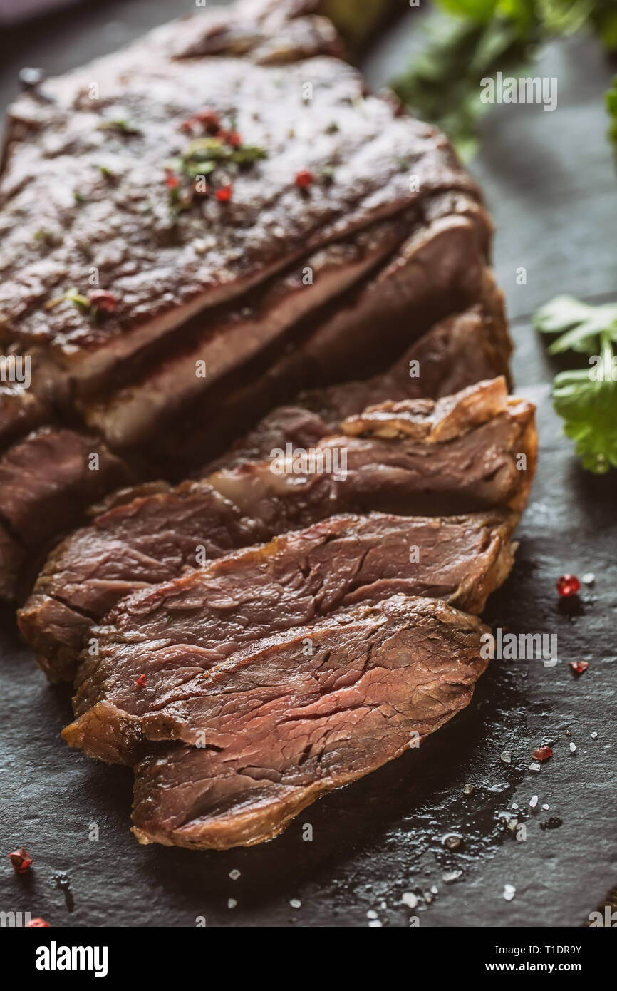 Frisch gegrilltes Rindersteak auf schiefer Teller mit Salz, Pfeffer, Rosmarin und Petersilie Kräuter. In Scheiben geschnittene Stücke von saftigen Rindersteak Stockfoto
