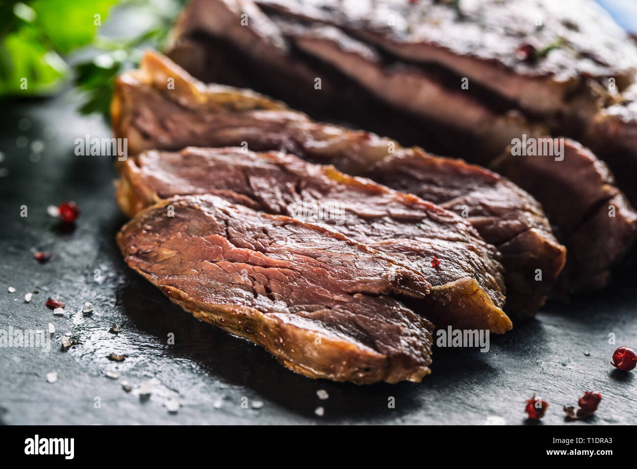 Frisch gegrilltes Rindersteak auf schiefer Teller mit Salz, Pfeffer, Rosmarin und Petersilie Kräuter. In Scheiben geschnittene Stücke von saftigen Rindersteak Stockfoto