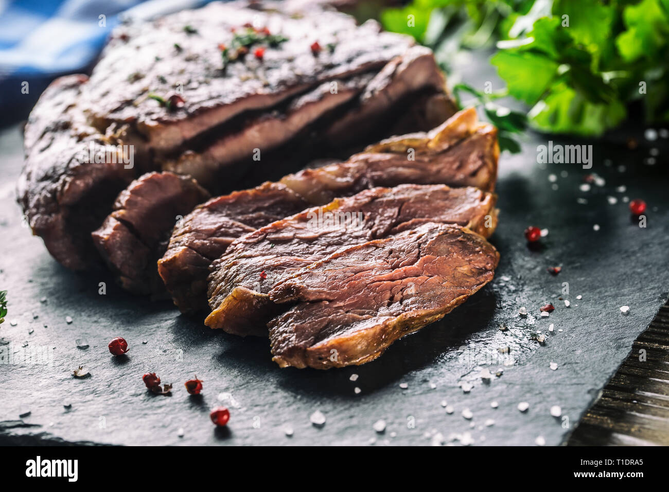 Frisch gegrilltes Rindersteak auf schiefer Teller mit Salz, Pfeffer, Rosmarin und Petersilie Kräuter. In Scheiben geschnittene Stücke von saftigen Rindersteak Stockfoto