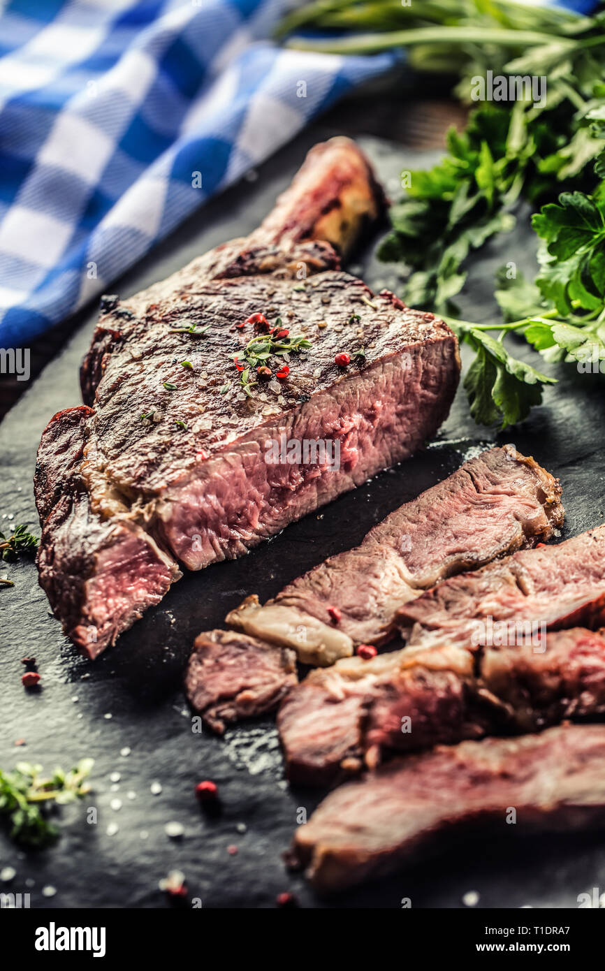 Frisch gegrillten Tomahawk Steak auf schiefer Teller mit Salz, Pfeffer, Rosmarin und Petersilie Kräuter. In Scheiben geschnittene Stücke von saftigen Rindersteak Stockfoto