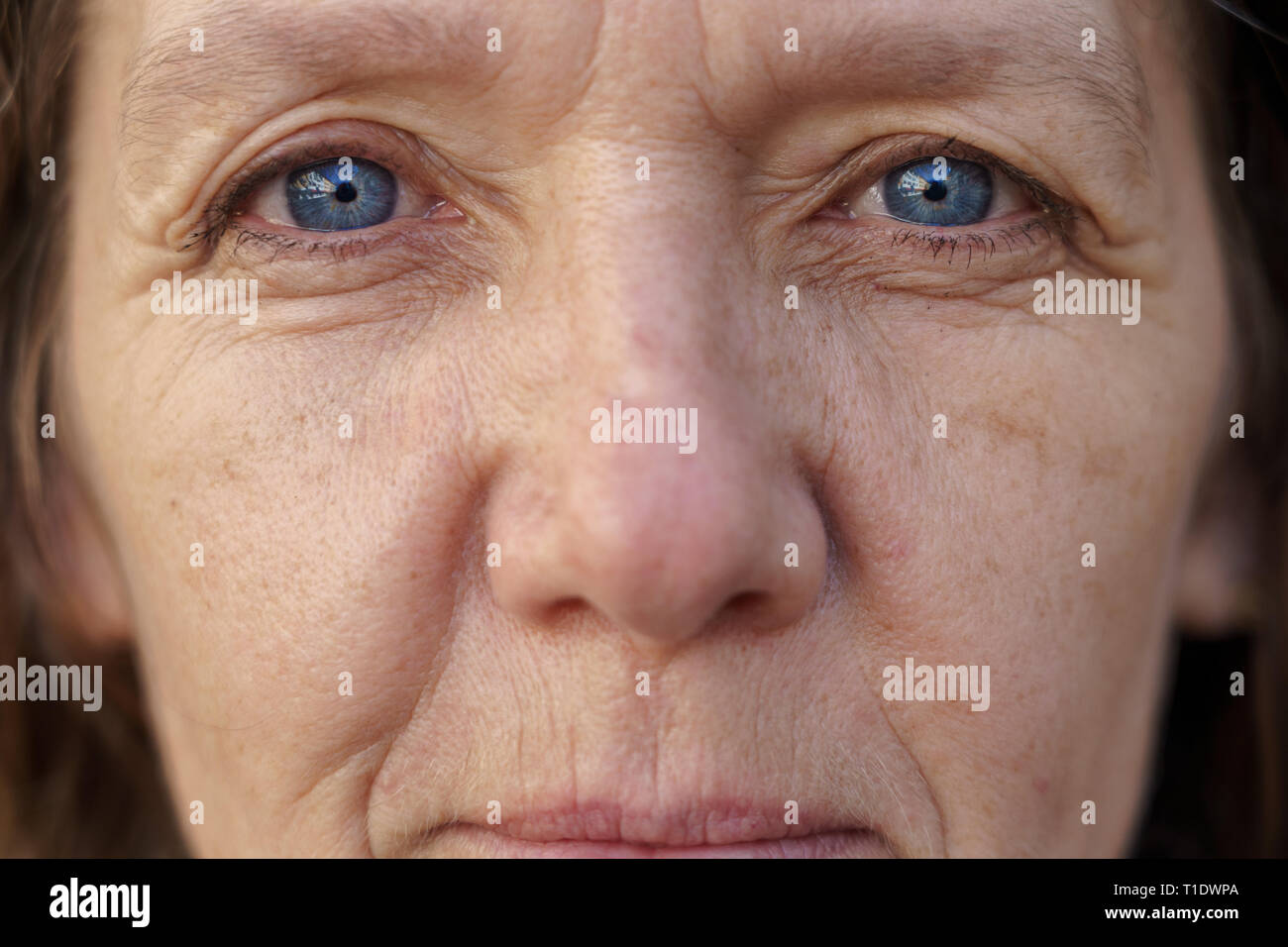 7/8 angesichts einer blauäugige Frau mittleren Alters mit faltige Haut suchen in die Linse in einem Konzept des Alterns Stockfoto