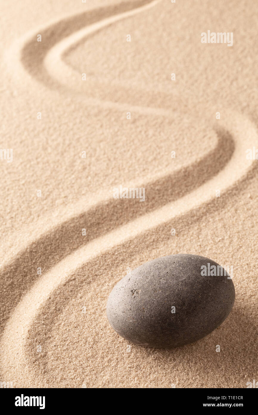 Gebogene Linie im Sand der Zen Stone Garten. Eine runde Black Rock auf sandigem Untergrund. Konzept für Spiritualität, Harmonie und Gleichgewicht. Stockfoto