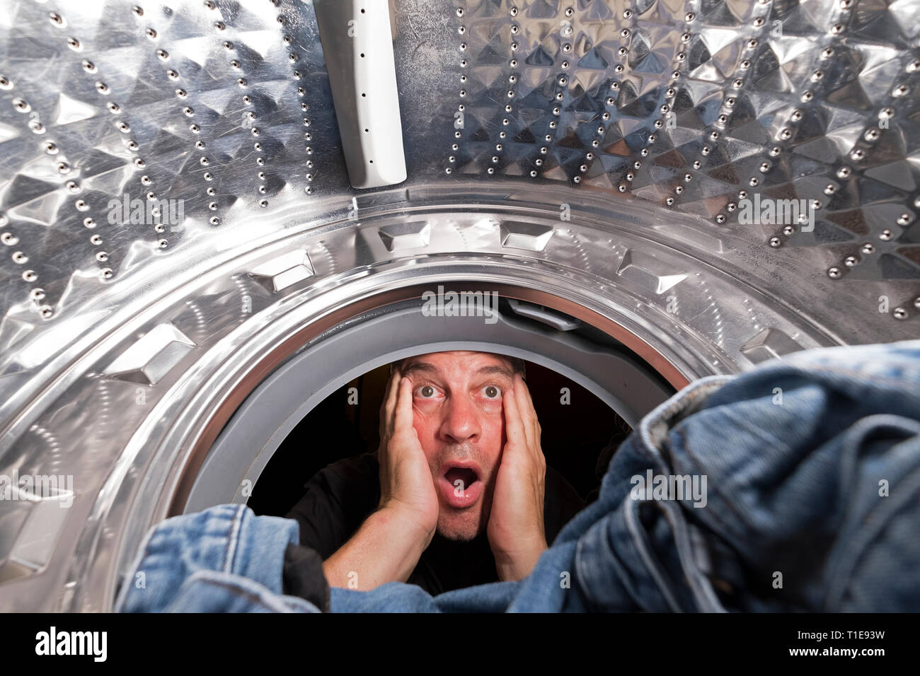 Waschtag. schockiert Mann sieht die Kleidung in die Waschmaschine Stockfoto