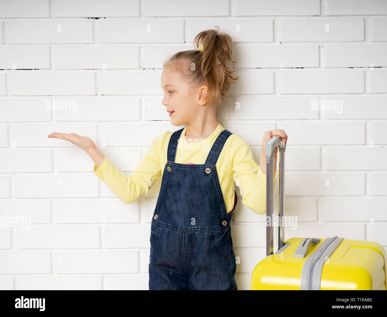 Kleine süße Mädchen mit einem gelben Koffer Reisetasche schaut sich etwas auf ihre Hand. Werbung. Reise Stockfoto
