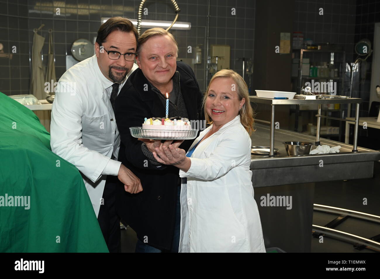 26. März 2019, Nordrhein-Westfalen, Köln: Die Schauspieler Jan Josef Liefers (L-R), Axel Prahl und Christine Urspruch stand in der Landschaft der gerichtlichen Medizin beim Fototermin am "Tatort Münster - Lakritz" (AT). Der Kuchen empfangen rühmen sich anlässlich seines Geburtstages. Foto: Horst Galuschka/dpa Stockfoto