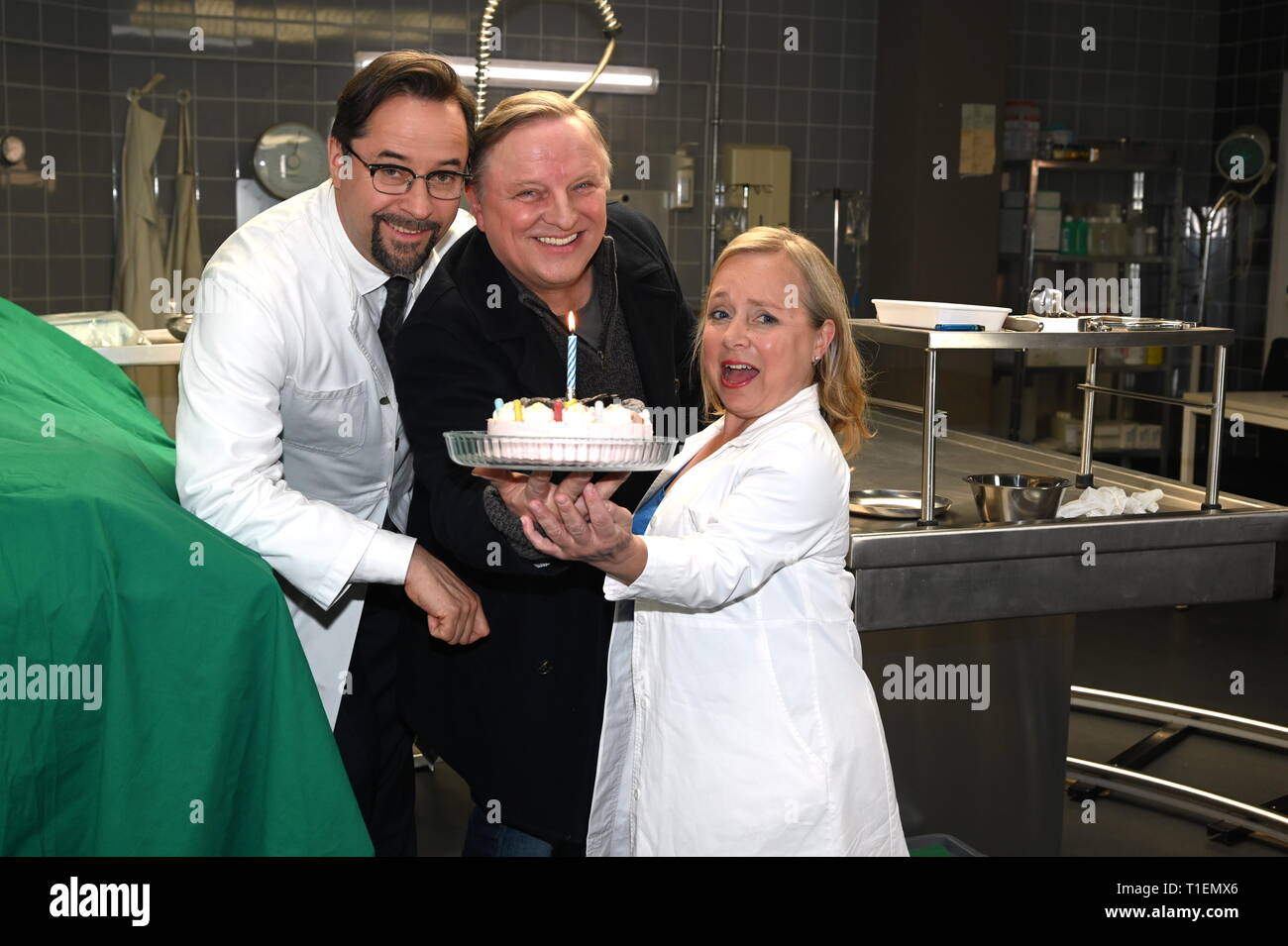 26. März 2019, Nordrhein-Westfalen, Köln: Die Schauspieler Jan Josef Liefers (L-R), Axel Prahl und Christine Urspruch stand in der Landschaft der gerichtlichen Medizin beim Fototermin am "Tatort Münster - Lakritz" (AT). Der Kuchen empfangen rühmen sich anlässlich seines Geburtstages. Foto: Horst Galuschka/dpa Stockfoto