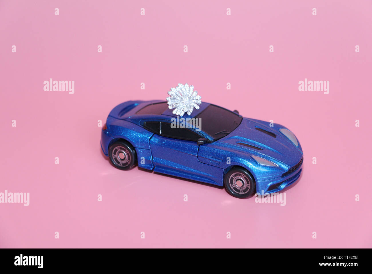 Die blauen Sportwagen trägt eine Crystal Blume. Die Gabe liegt auf dem Dach des Autos. Rosa Hintergrund. Spielzeug für Kinder. Es gibt keine Menschen. Stockfoto