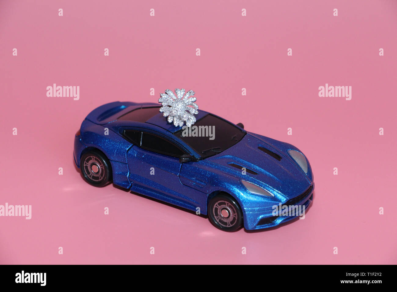Die blauen Sportwagen trägt eine Crystal Blume. Die Gabe liegt auf dem Dach des Autos. Rosa Hintergrund. Spielzeug für Kinder. Es gibt keine Menschen. Stockfoto