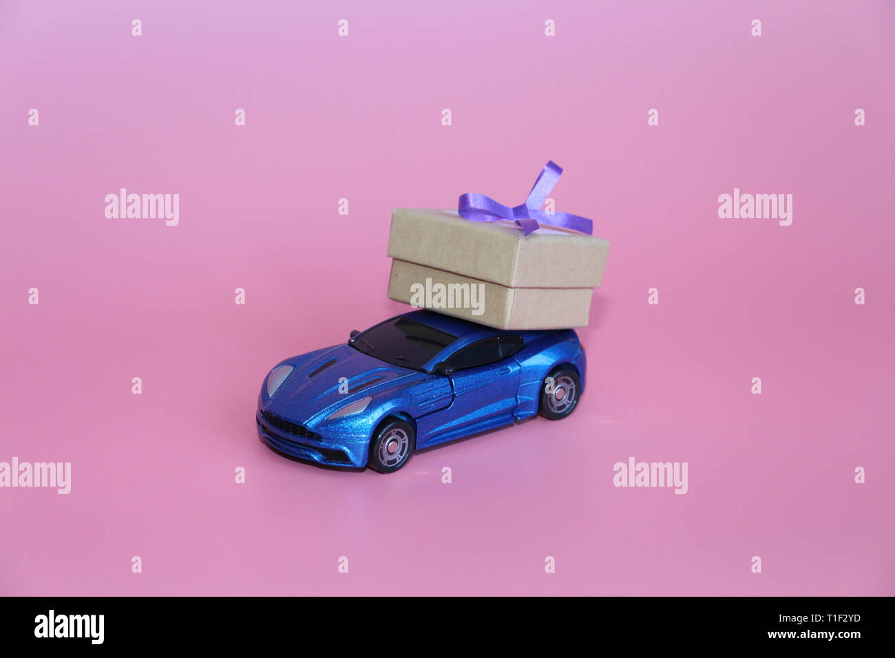 Blaue Sportwagen trägt eine Geschenkbox. Die Gabe liegt auf dem Dach des Autos. Rosa Hintergrund. Der 14. Februar. März 8. Spielzeugauto. Stockfoto