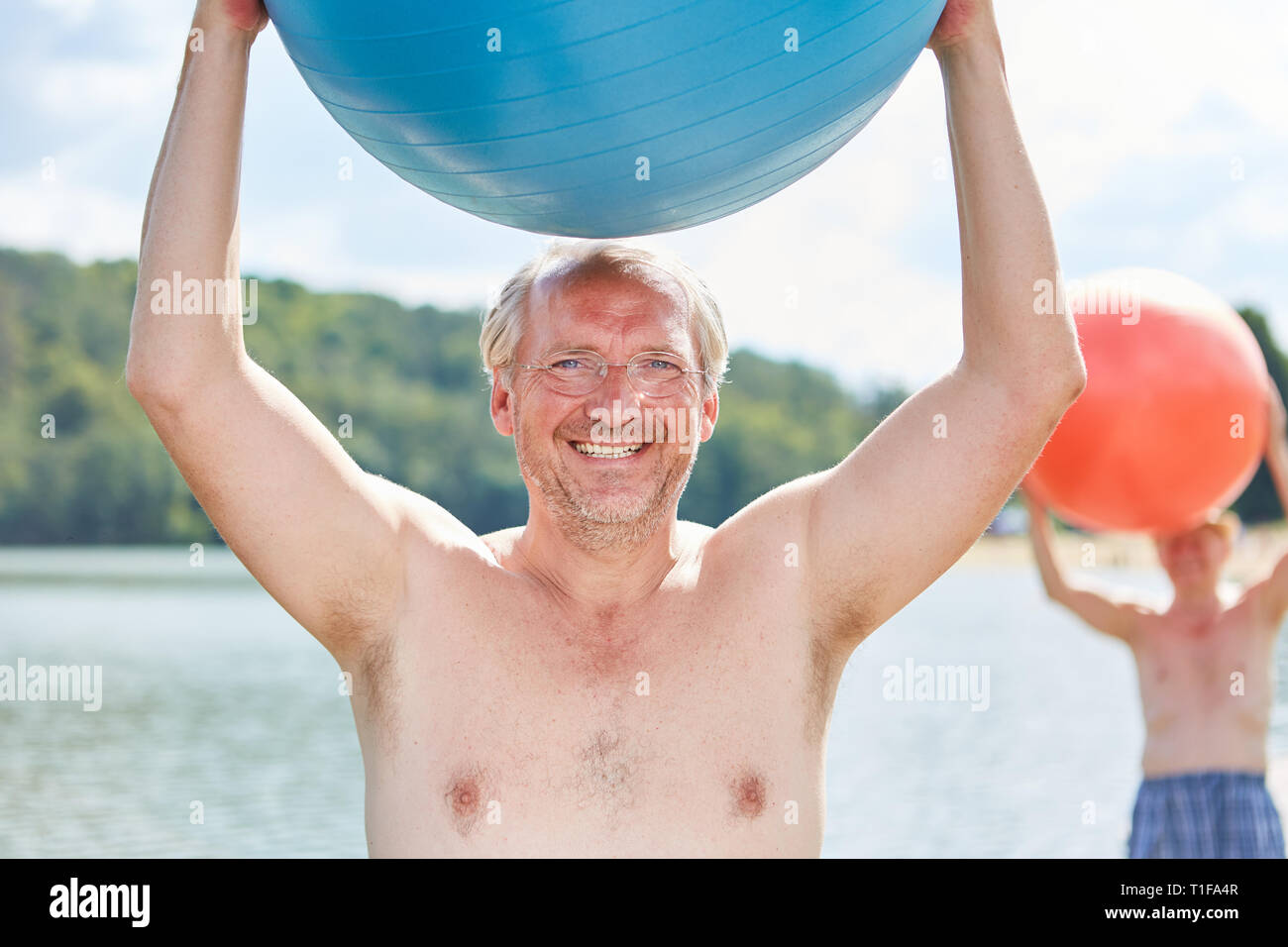 Vital älterer Mann mit einem Gymnastikball Gymnastik am See im Sommer Stockfoto