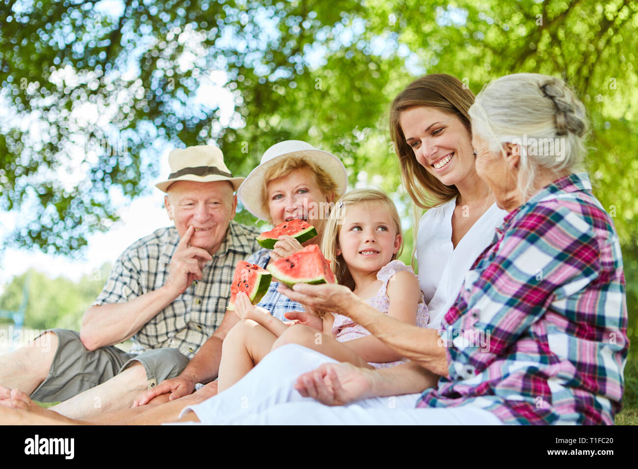 Erweiterte Familie mit Kind und Großeltern essen Melone im Sommer im Garten Stockfoto