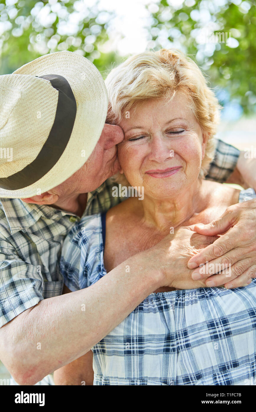 Älterer Mann zärtlich umarmt und küsst seine Frau im Sommer auf Urlaub in der Natur Stockfoto