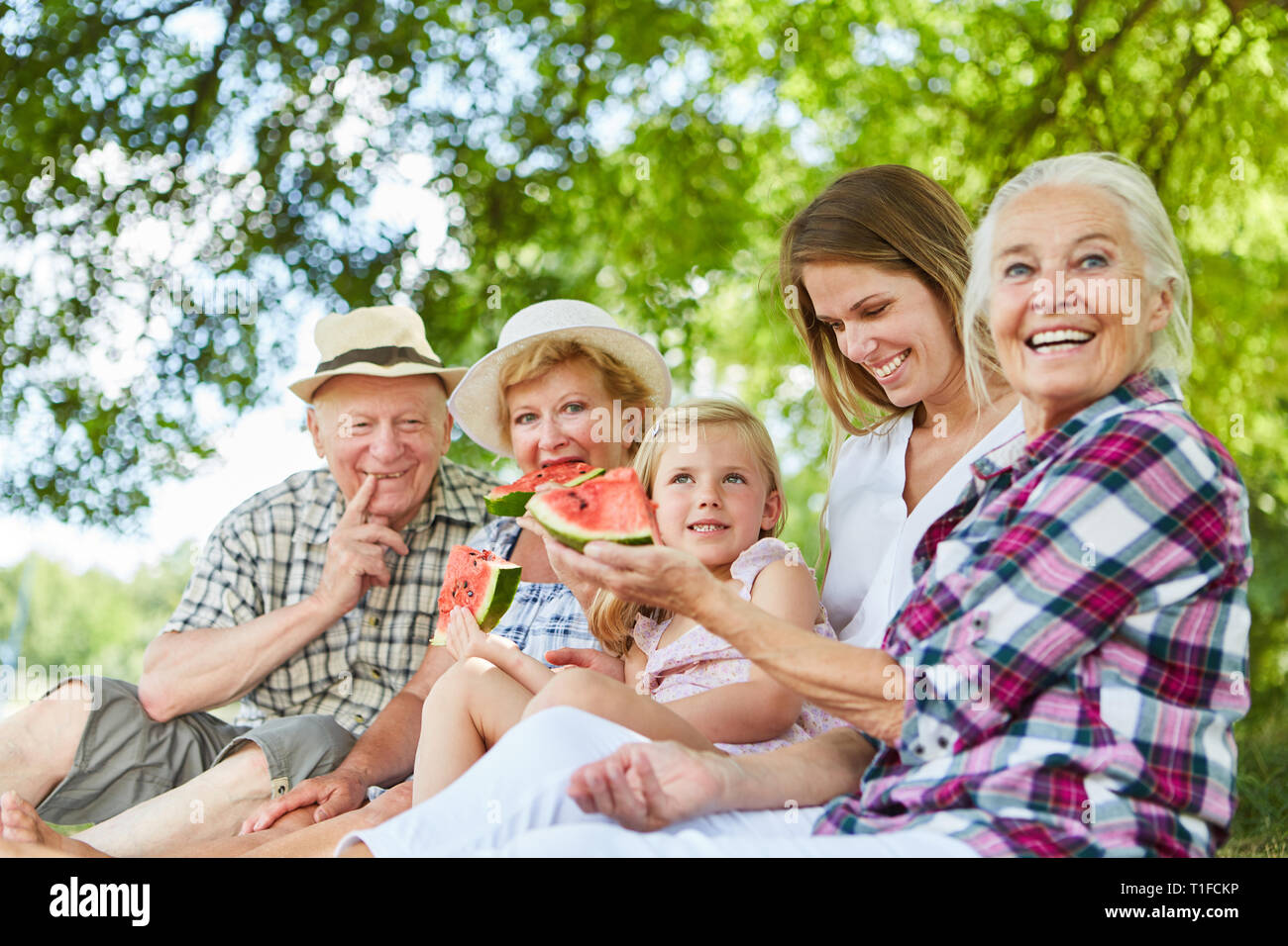 Glückliche Familie mit Kind und Großeltern beim Essen Melone im Park im Sommer Stockfoto