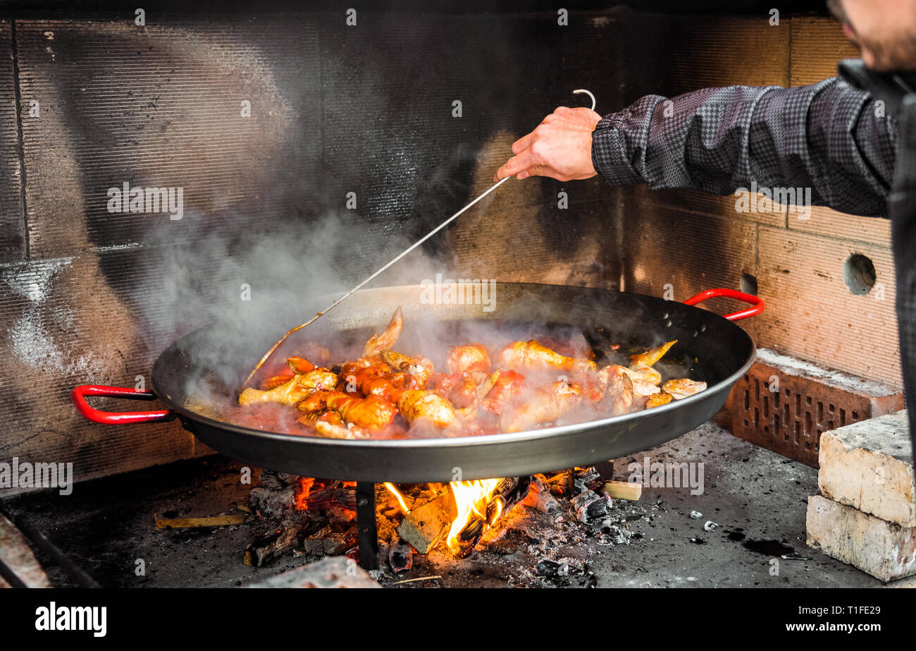 Kochen und eine traditionelle spanische Paella über offenem Feuer. Die traditionelle Art der Vorbereitung valencianische Paella mit Feuer und Flamme in einem großen Topf. Stockfoto