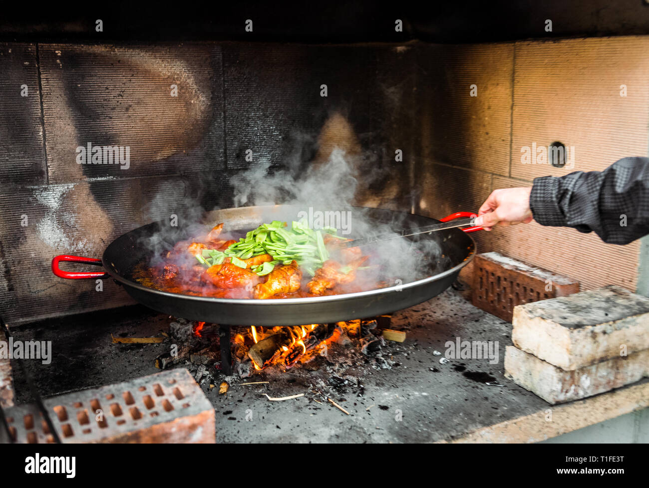 Kochen und eine traditionelle spanische Paella über offenem Feuer. Die traditionelle Art der Vorbereitung valencianische Paella mit Feuer und Flamme in einem großen Topf. Stockfoto