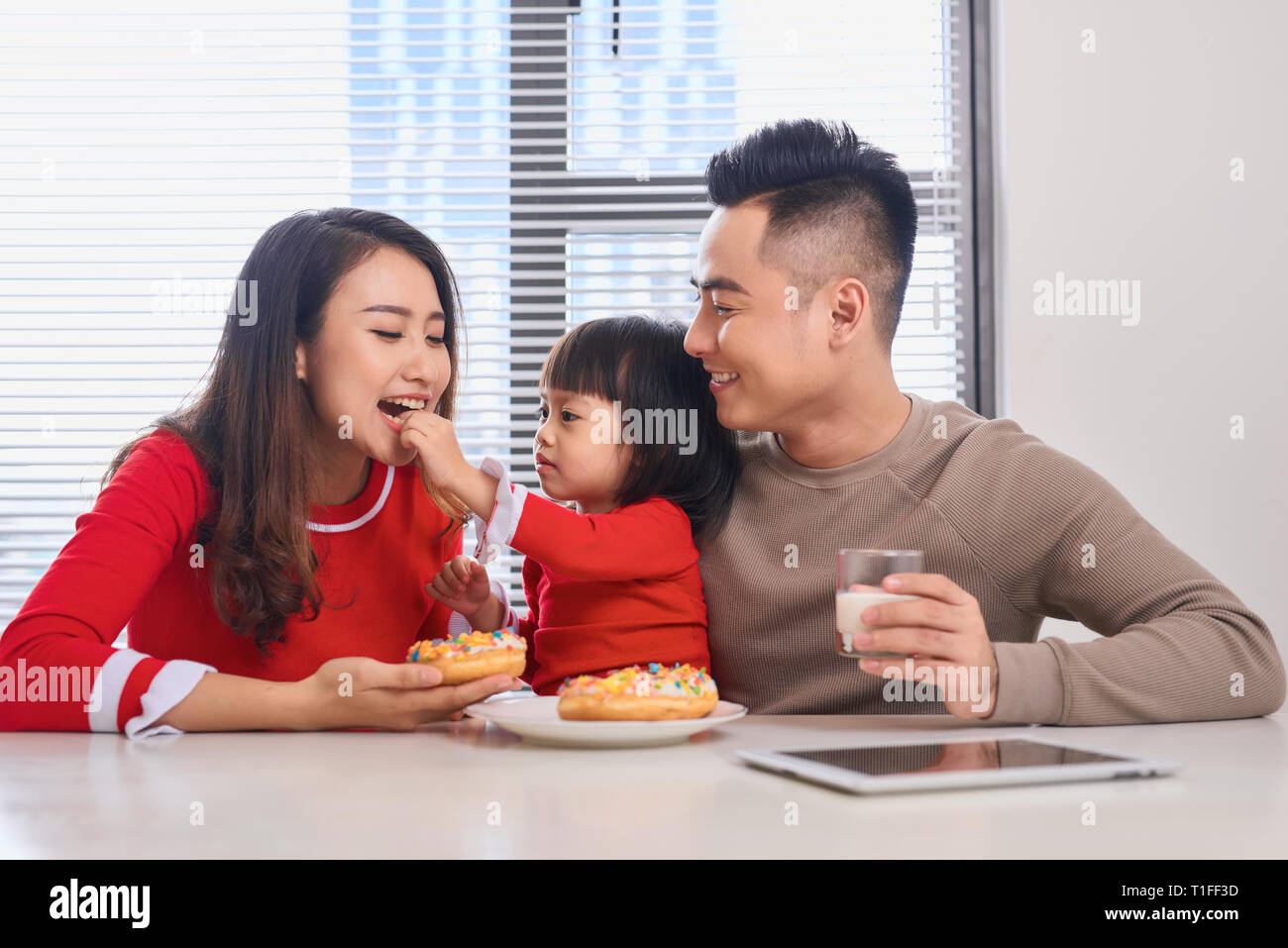 Glückliche junge Familie mit Kindern genießen Sie das Frühstück in einem weißen sonnigen Speisesaal mit großem Garten Fenster Ansicht. Stockfoto