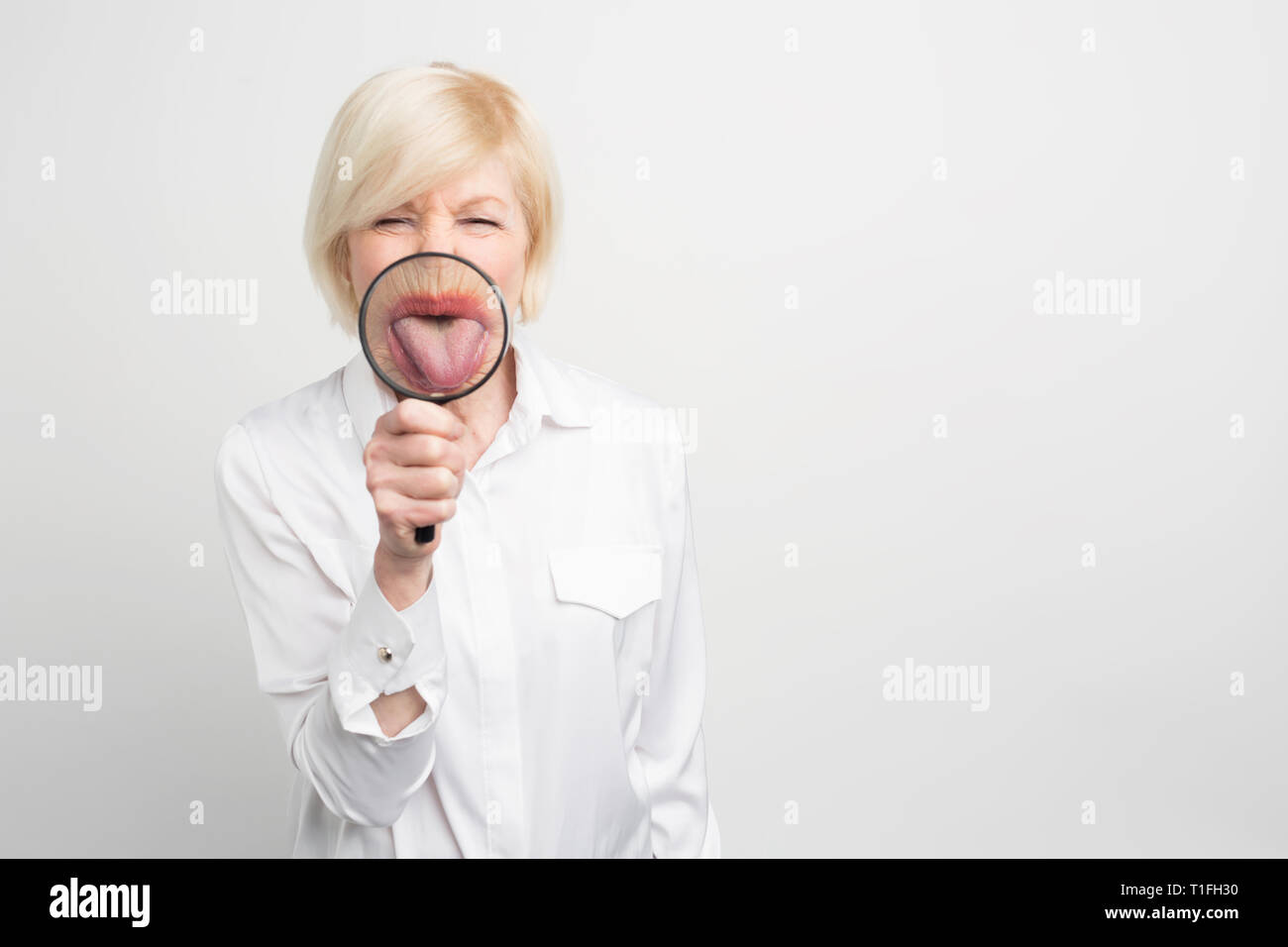 Nahaufnahme von lustige Frau in weißer Bluse mit einer Zunge durch die Lupe. Auf weissem Hintergrund. Stockfoto