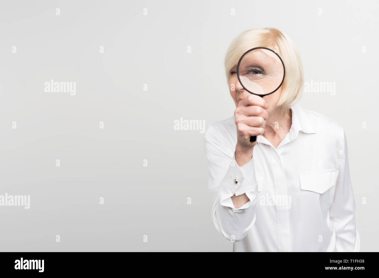 Ein Bild der weißhaarige Frau, die auf der rechten Seite des Rahmens und geradeaus Blick durch die Lupe. Auf weissem Hintergrund. Stockfoto