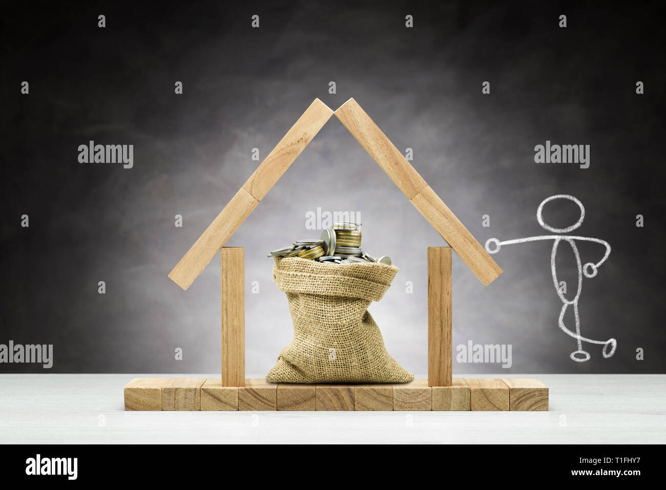 Konzept des Schutzes, Holzhaus auf grauem Hintergrund mit Beutel voller Münzen unter dem Dach. Stockfoto
