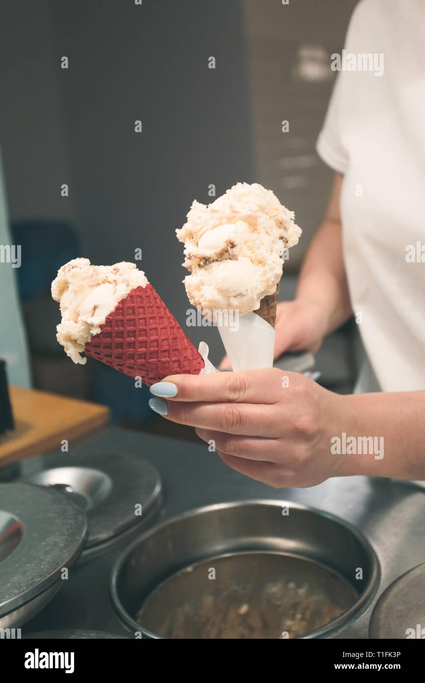 Verkäufer der Verkauf ein paar Kugeln Eis in einem Candy Shop durch eine Straße. Frau setzen einer Kugeln Eis zu einem Kegel Stockfoto