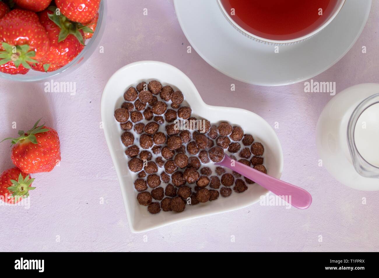 Kakao Kugeln Getreide in Weiß in Herzform Schüssel als Teil der kompletten Frühstück einschließlich Erdbeeren, Milch und Tasse rote Früchte Tee. Von oben nach unten Stockfoto