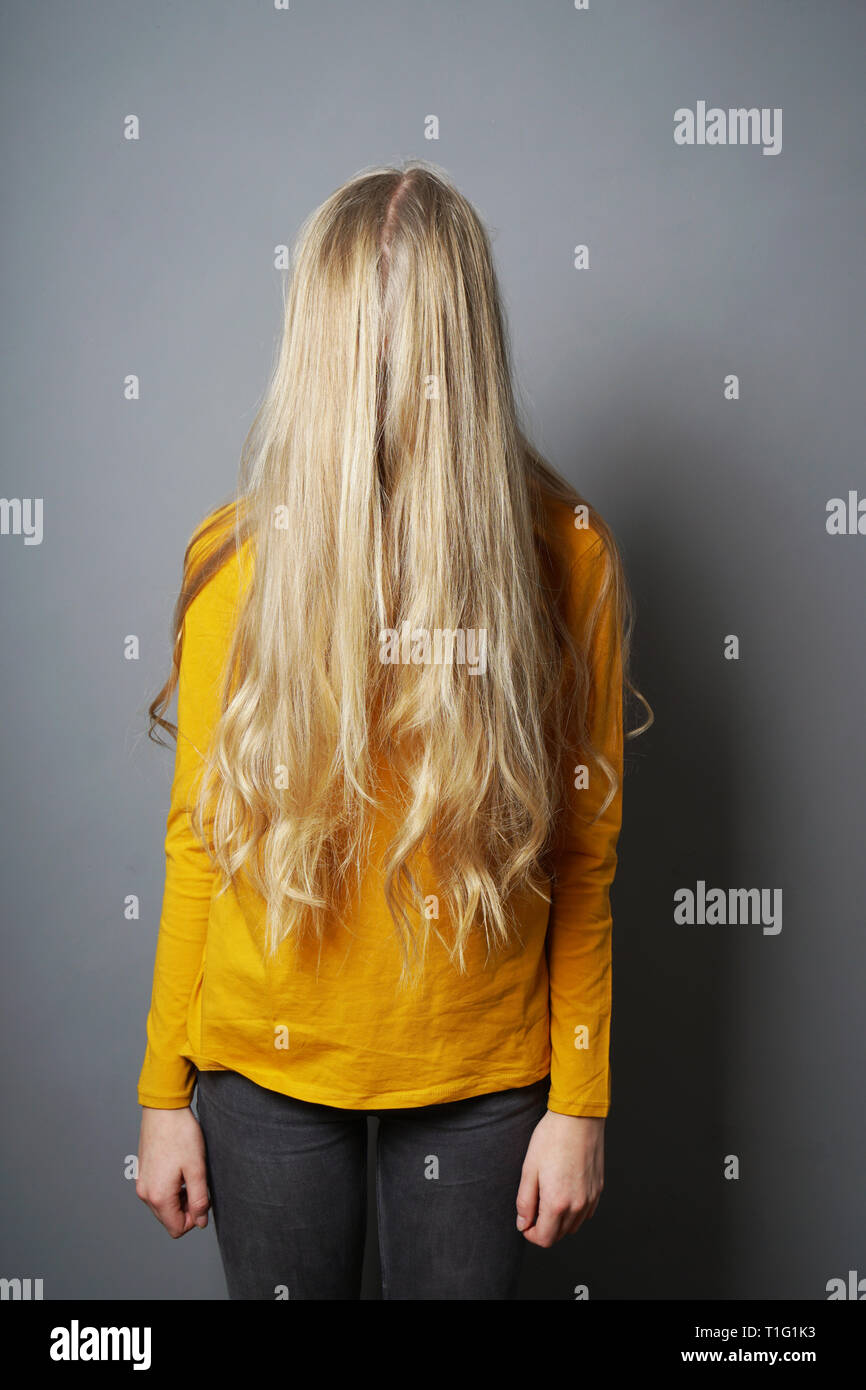 Schüchterne junge Frau mit verdunkelte Gesicht hinter langen blonden Haaren Stockfoto