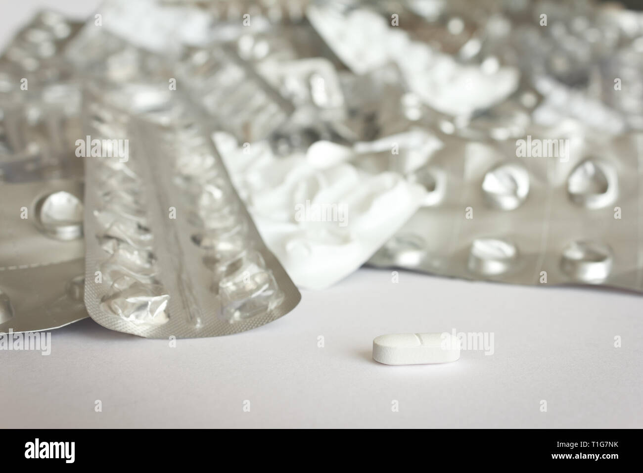 Eine einzige Tablette vor vielen leeren blister Pakete auf weißem Hintergrund, Drogenmissbrauch Konzept. Stockfoto