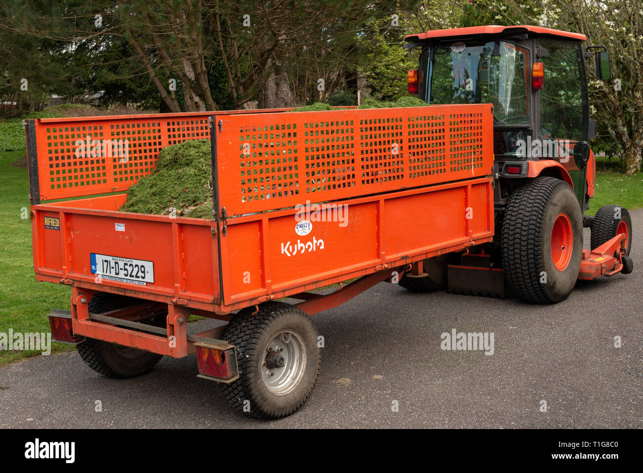 Orangefarbener Minitraktor und Anhänger voller frisch geschnittenem Gras im Muckross House Estate and Gardens, Killarney National Park, County Kerry, Irland Stockfoto