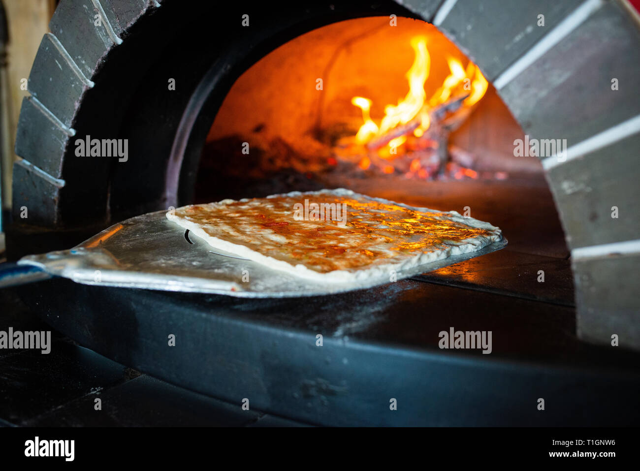 Im römischen Stil italienische Pizza auf Peel Spaten über in einen Wald zu setzen, die für das Kochen in einer Trattoria/restaurant/pizzeria Brennofen. Stockfoto